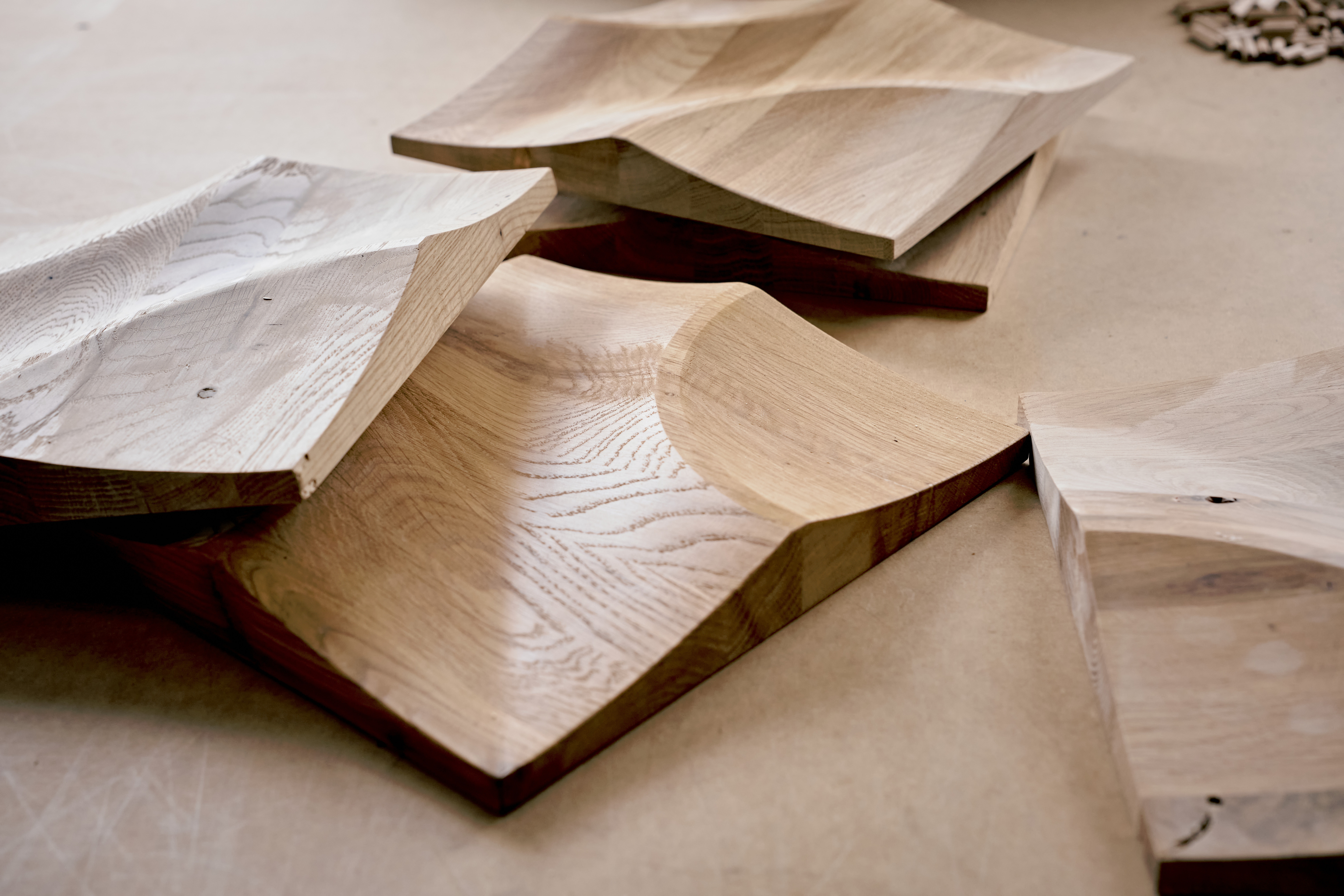 Geformte Holzplatten mit organischen Wellenstrukturen liegen auf einer Werkbank, verschiedene Maserungen und Holzfarben sichtbar